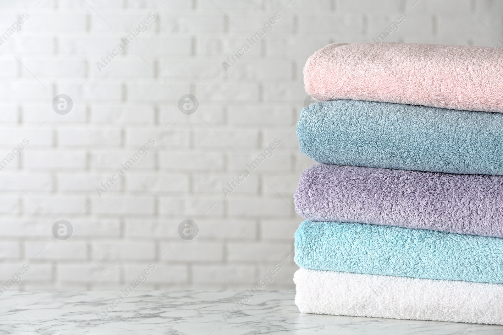 Photo of Stack of clean bath towels on white marble table. Space for text