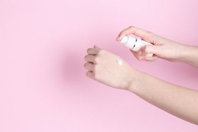 Photo of Woman applying cream on her hand against pink background, closeup. Space for text