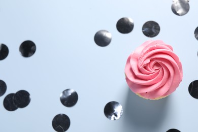 Photo of Delicious cupcake with bright cream and confetti on light background, flat lay