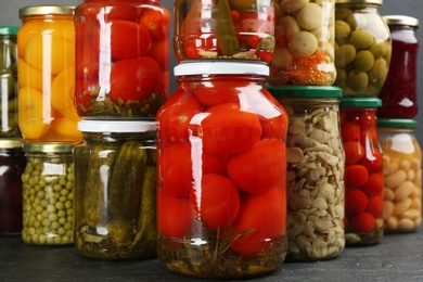 Photo of Jars of pickled vegetables on grey table, closeup