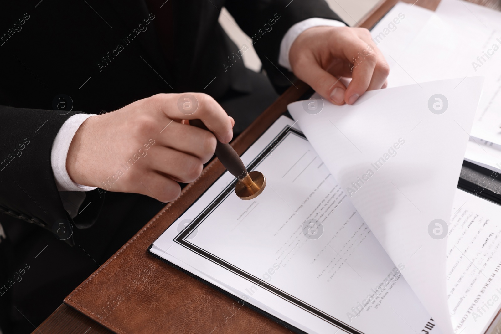 Photo of Notary stamping document at table in office, closeup