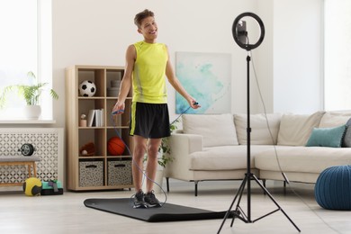 Photo of Smiling sports blogger jumping with rope while streaming online fitness lesson with smartphone at home