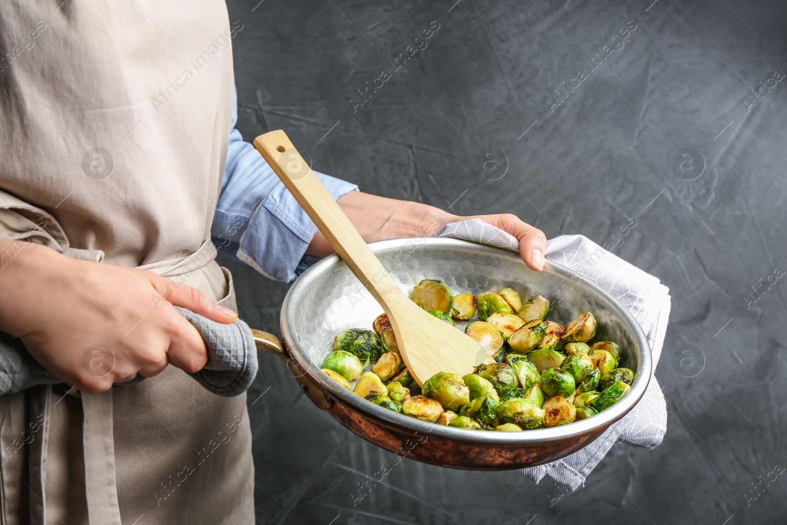 Photo of Woman with frying pan of roasted Brussels sprouts on grey background, closeup