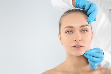Photo of Doctor examining young woman face before cosmetic surgery on white background. Space for text