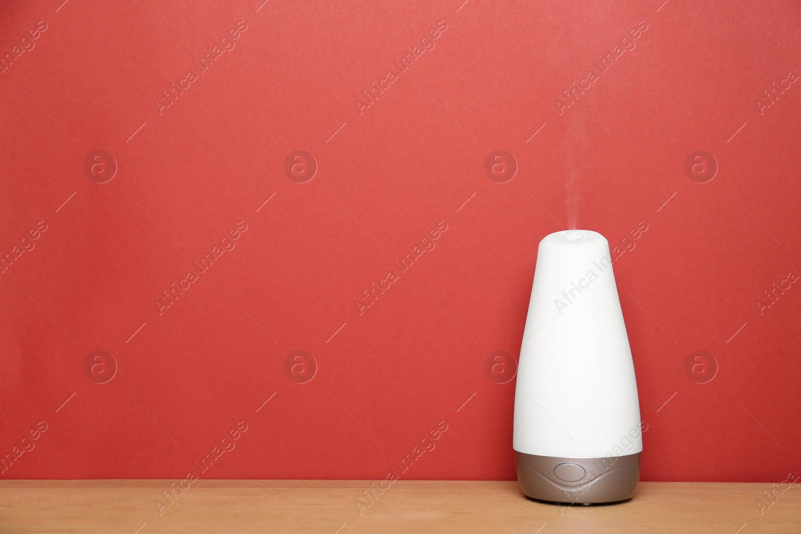 Photo of Essential oils diffuser on wooden table near red wall. Space for text