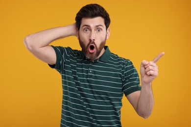 Surprised man pointing at something on yellow background