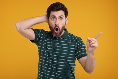 Photo of Surprised man pointing at something on yellow background