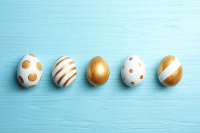 Photo of Set of traditional Easter eggs decorated with golden paint on wooden background, top view