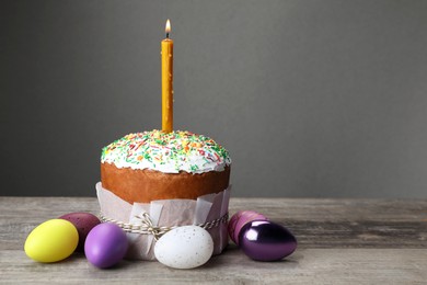 Photo of Traditional Easter cake with sprinkles, burning candle and painted eggs on wooden table, space for text