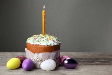 Traditional Easter cake with sprinkles, burning candle and painted eggs on wooden table, space for text