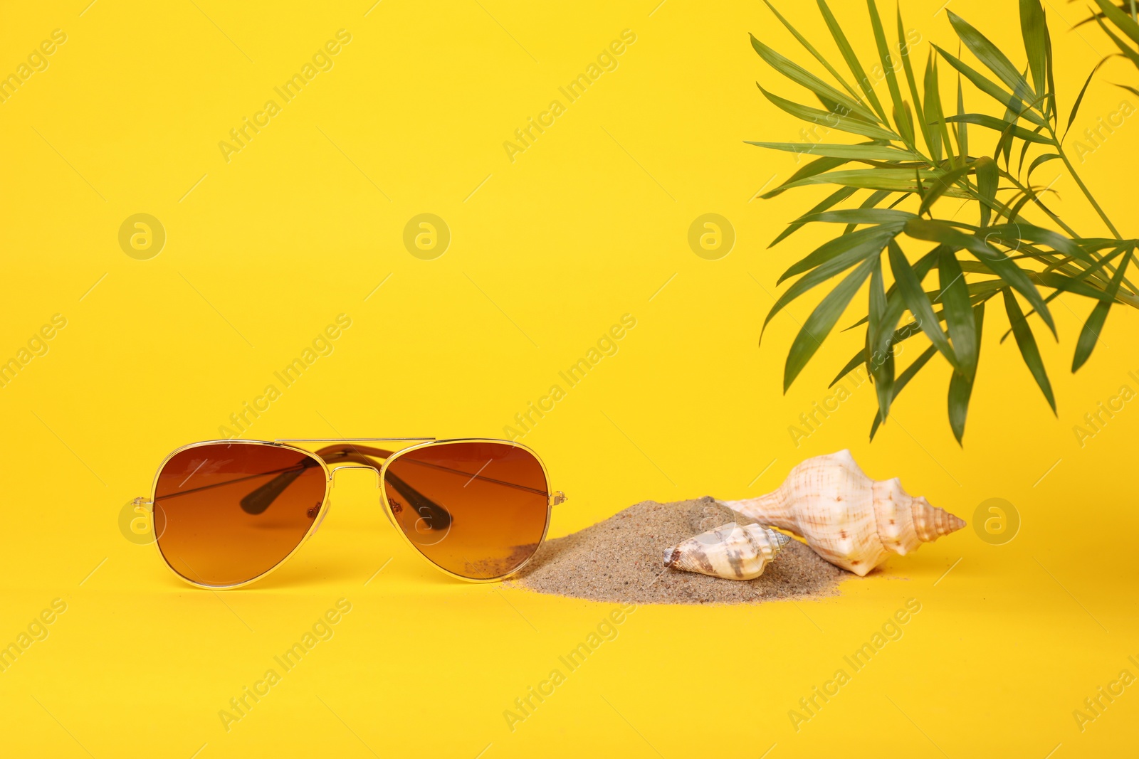 Photo of Stylish sunglasses, seashells, sand and palm leaves on yellow background