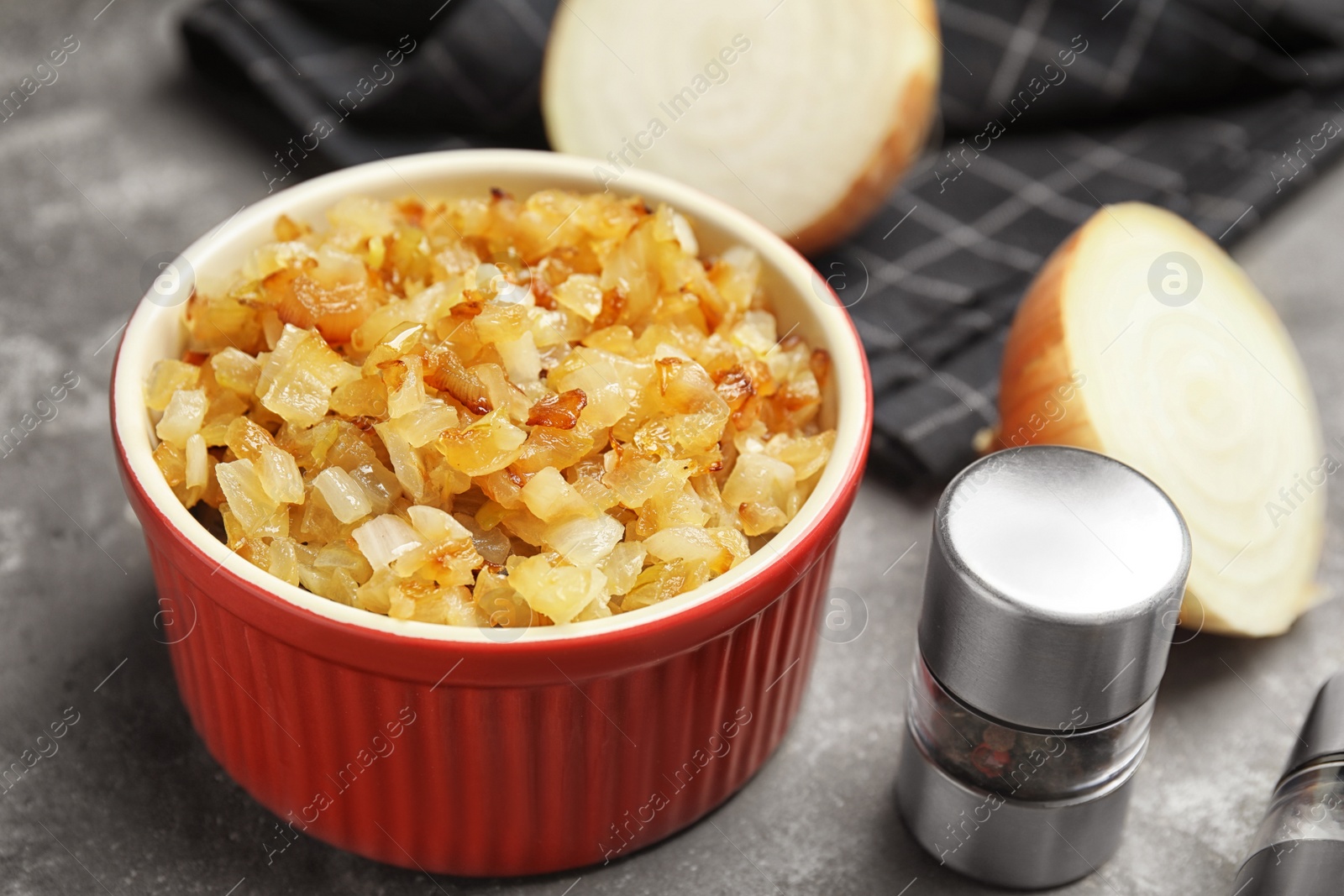 Photo of Tasty fried onion and pepper shaker on grey table, closeup