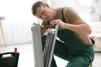 Professional technician repairing electric ultrared heater with screwdriver indoors