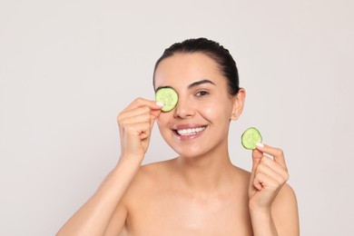 Photo of Beautiful young woman putting slices of cucumber on eyes against light grey background