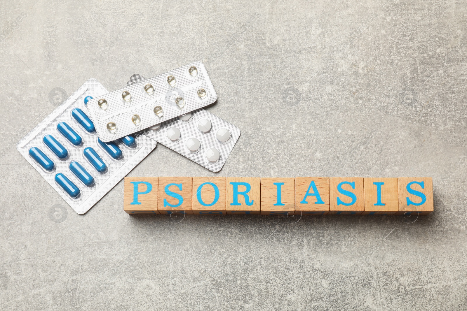 Photo of Word Psoriasis made of wooden cubes with letters and pills on light gray textured table, flat lay