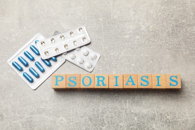 Word Psoriasis made of wooden cubes with letters and pills on light gray textured table, flat lay