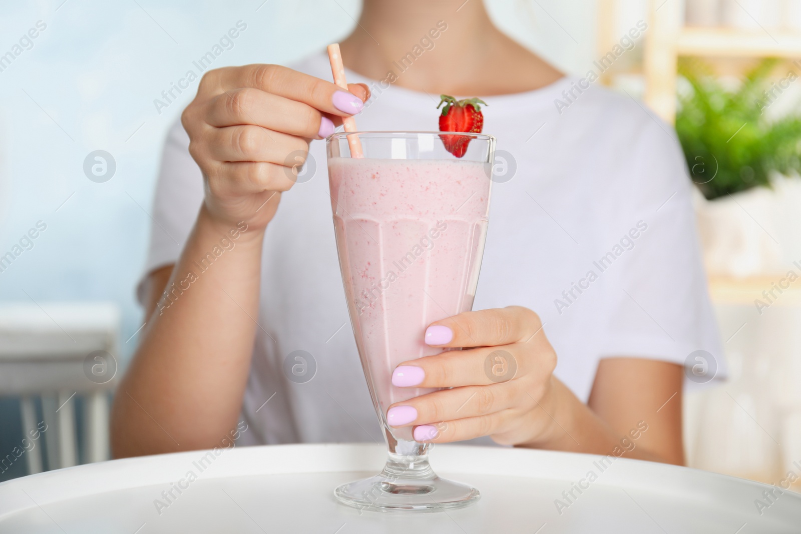 Photo of Woman holding tasty fresh milk shake with strawberry at table indoors, closeup