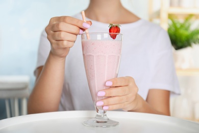 Photo of Woman holding tasty fresh milk shake with strawberry at table indoors, closeup