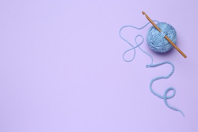 Photo of Clew of light blue knitting thread and crochet hook on violet background, top view. Space for text