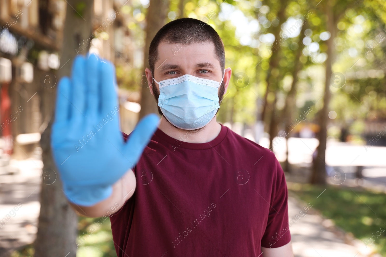 Photo of Man in protective face mask showing stop gesture outdoors. Prevent spreading of coronavirus