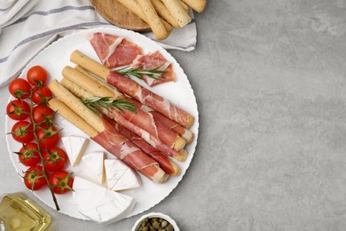 Photo of Delicious grissini sticks with prosciutto and snacks on grey table, flat lay. Space for text