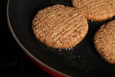 Cooking vegan cutlets in frying pan on cooktop, closeup