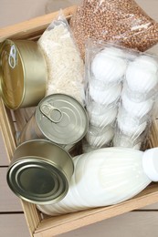 Donation box with food products on wooden table, top view