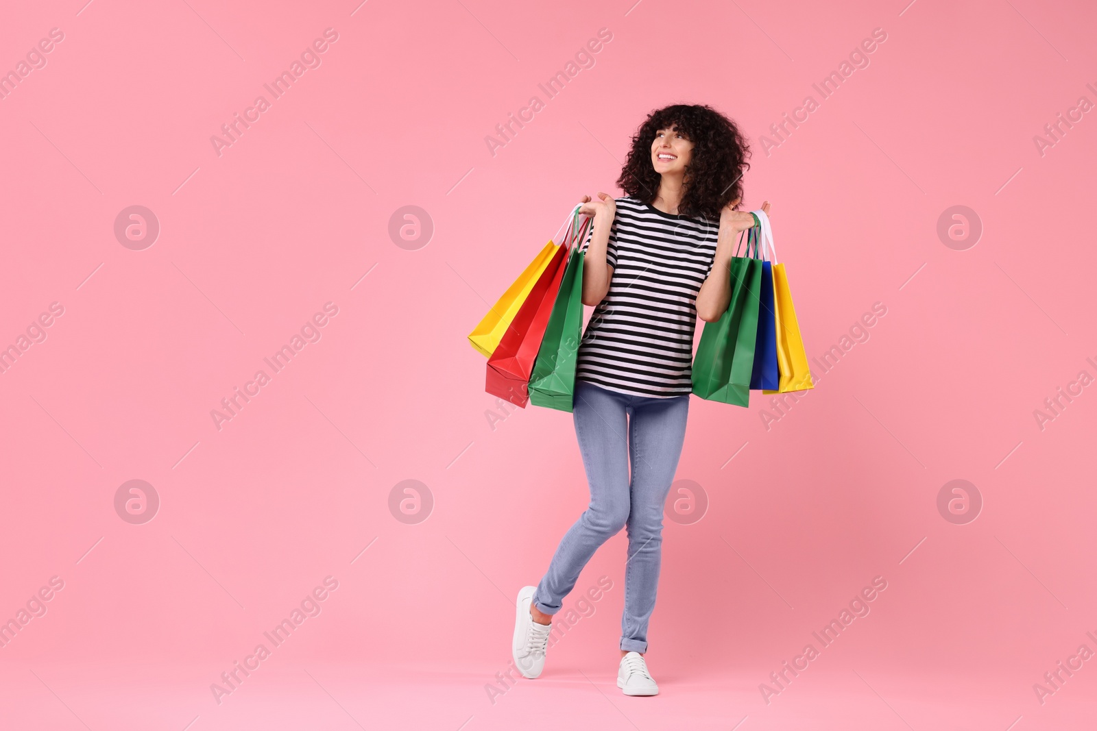 Photo of Happy young woman with shopping bags on pink background