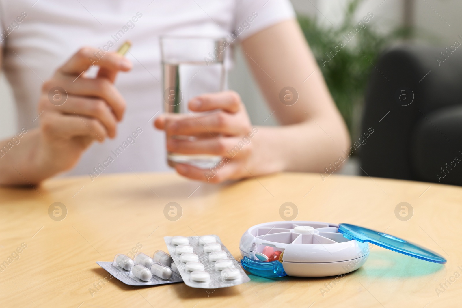 Photo of Woman with pills, organizer and glass of water at light wooden table, selective focus