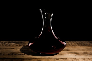 Photo of Elegant decanter with red wine on table against dark background