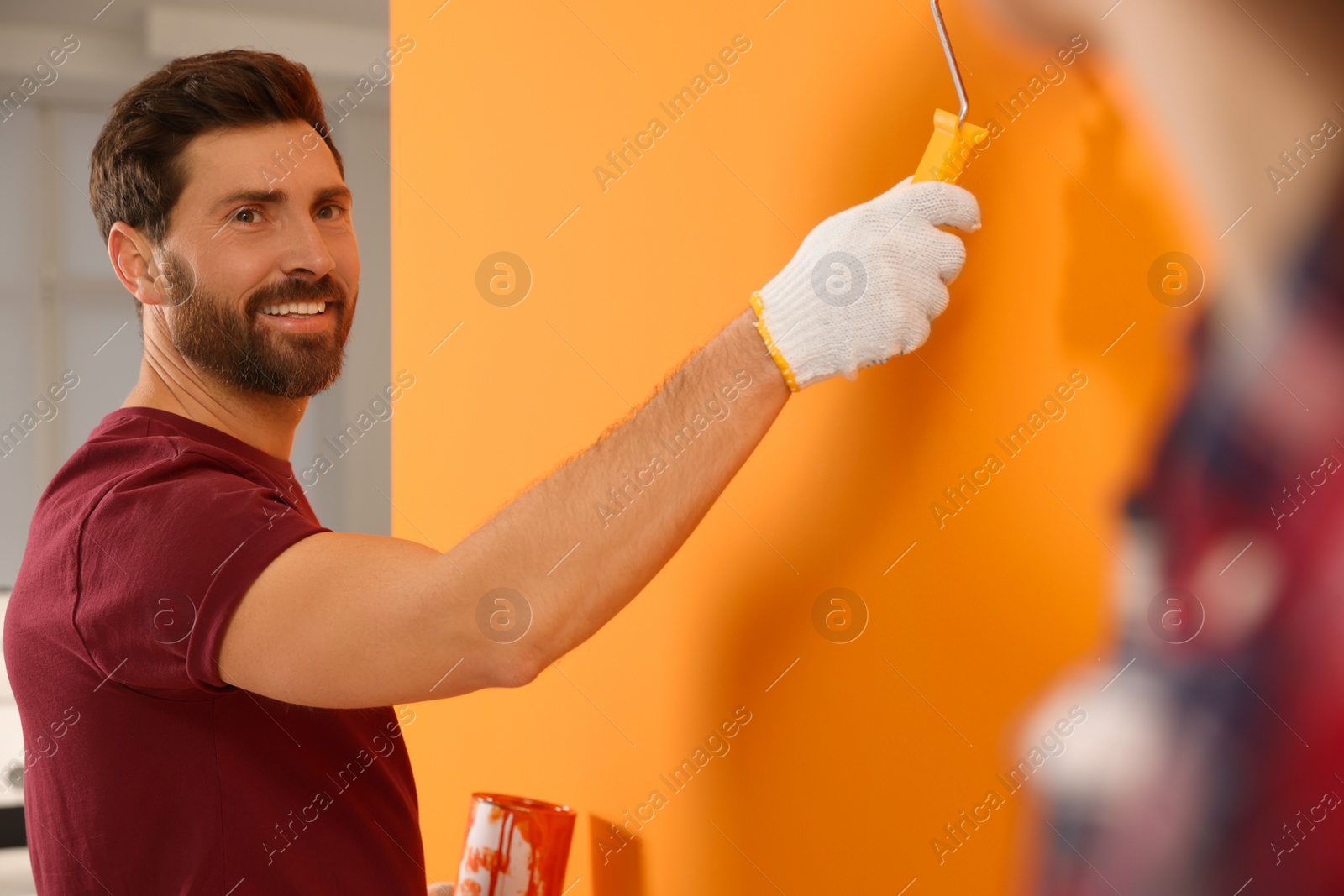 Photo of Happy designer painting orange wall with roller