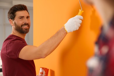 Happy designer painting orange wall with roller