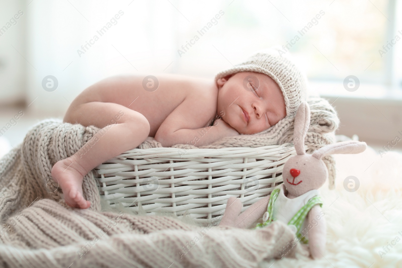 Photo of Adorable newborn baby lying in basket with knitted plaid indoors