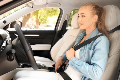 Photo of Female driver fastening safety belt in car