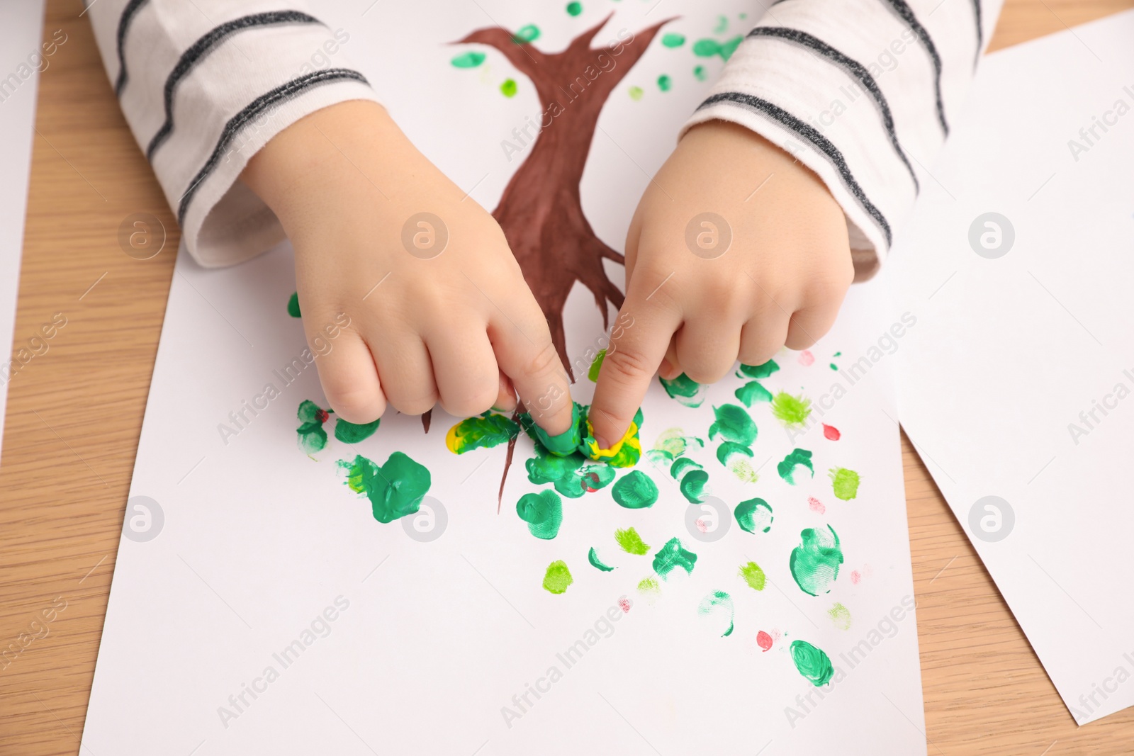Photo of Little child painting with fingers at wooden table , closeup