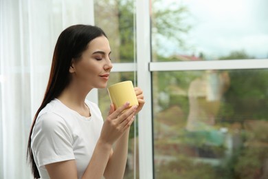Photo of Young woman with cup of drink relaxing near window home, space for text