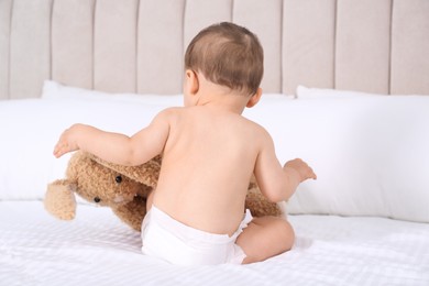 Photo of Cute baby in dry soft diaper with toy bunny on white bed at home, back view
