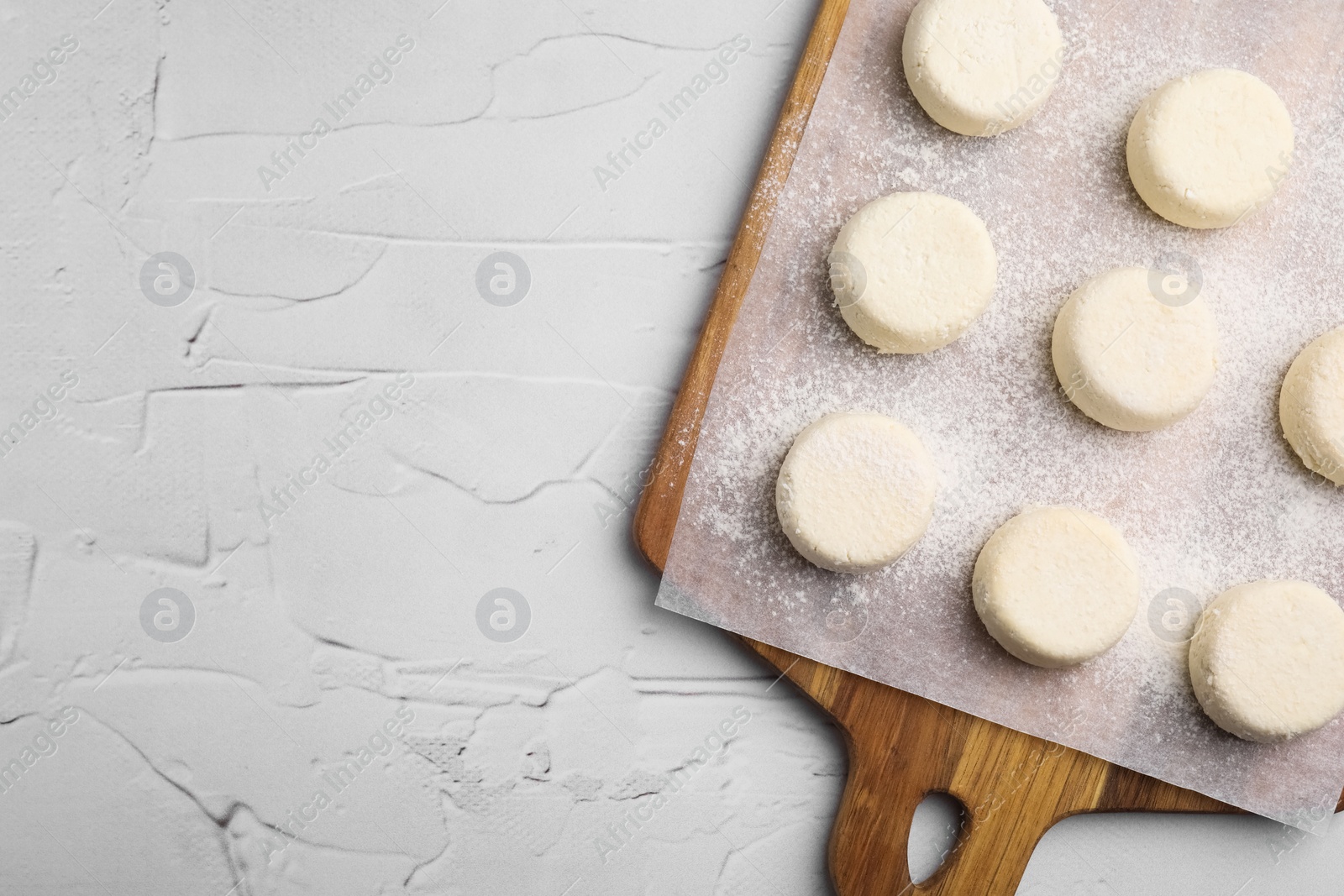 Photo of Wooden board with uncooked cottage cheese pancakes on white textured table, top view. Space for text