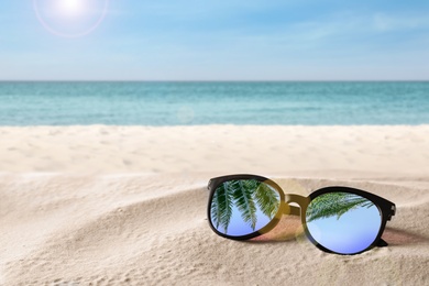 Green palm leaves reflecting in sunglasses on sandy beach near ocean