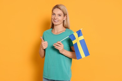 Photo of Woman with flag of Sweden showing thumb up on yellow background