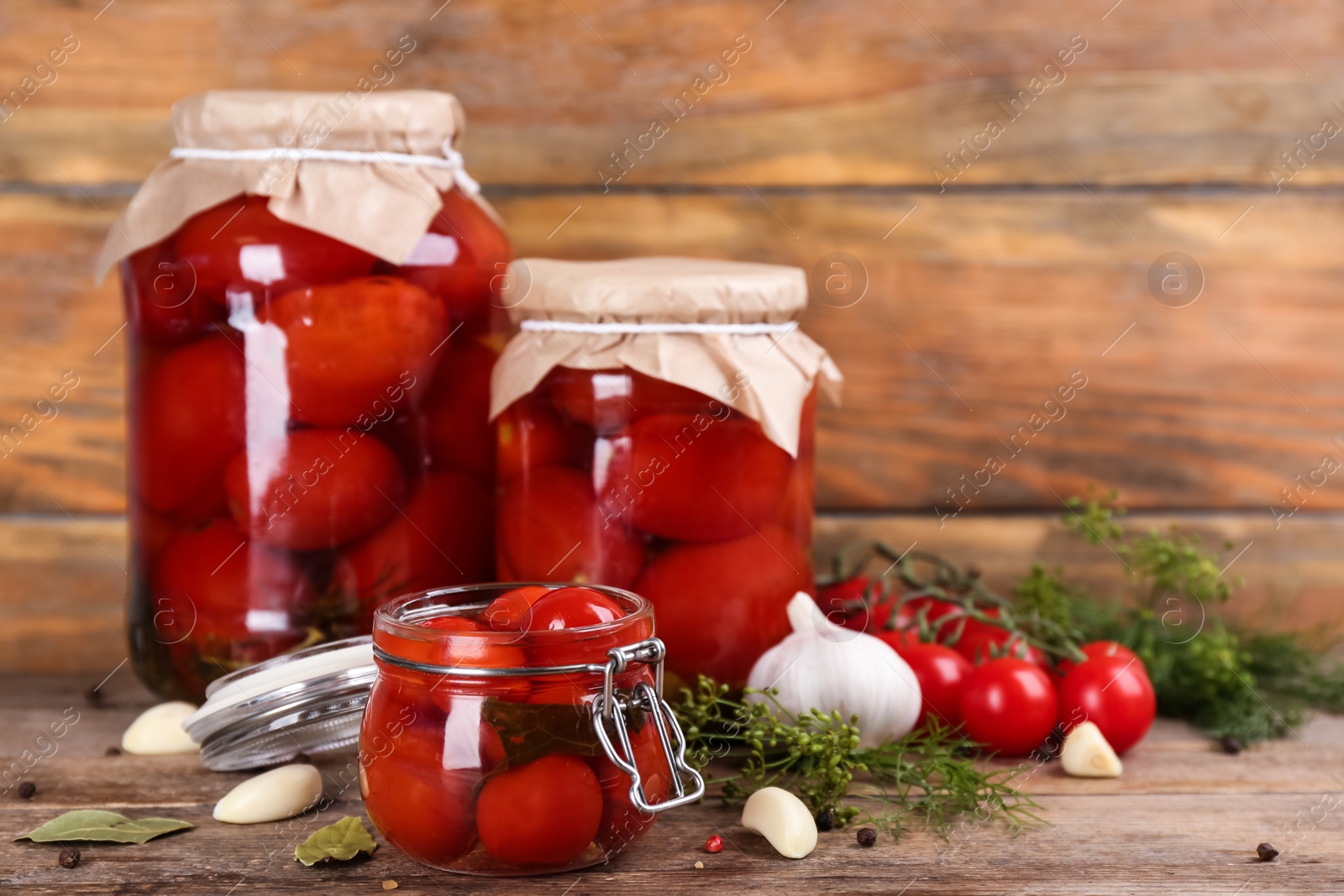 Photo of Glass jars of pickled tomatoes and ingredients on wooden table. Space for text