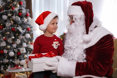 Santa Claus giving present to little boy in room decorated for Christmas