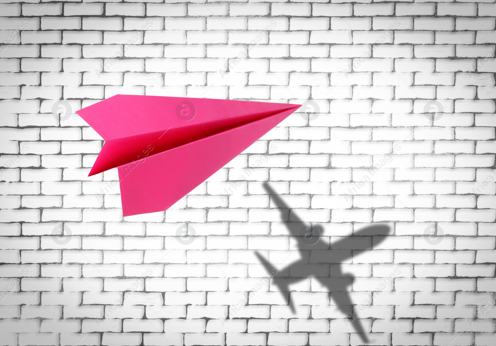 Image of Flying paper plane and shadow of a real airplane on white brick wall