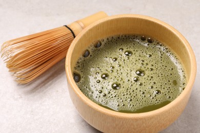 Photo of Bowl of fresh matcha tea and bamboo whisk on light table, closeup