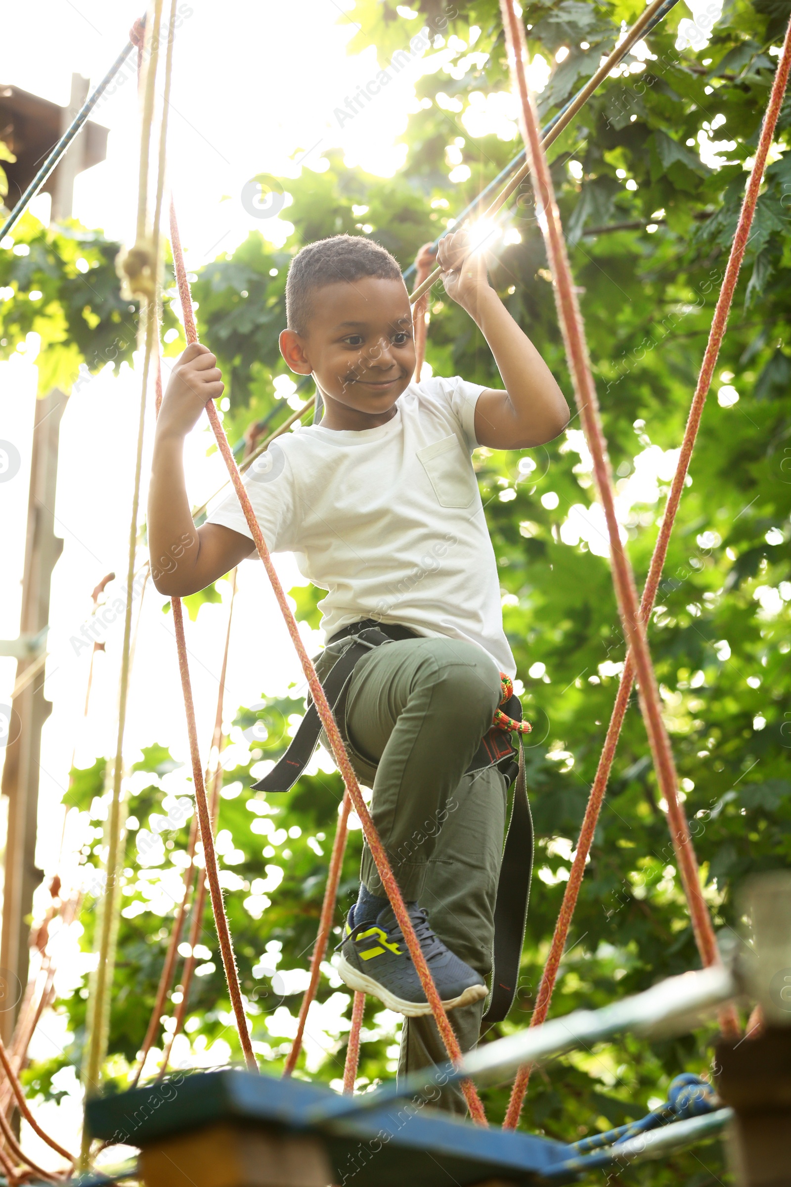 Photo of Little African-American boy climbing in adventure park. Summer camp