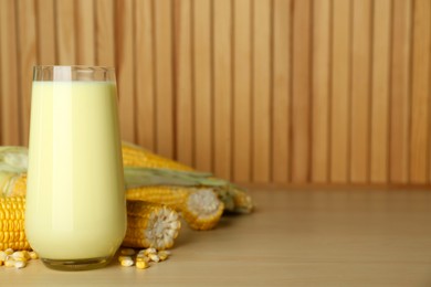 Photo of Tasty fresh corn milk in glass and cobs on wooden table. Space for text