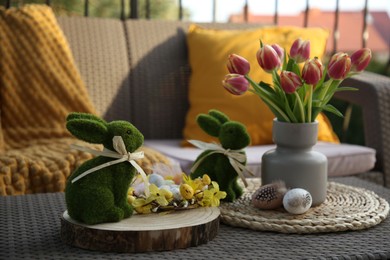 Photo of Terrace with Easter decorations. Bouquet of tulips in vase, bunny figures, decorative nest and eggs on table outdoors