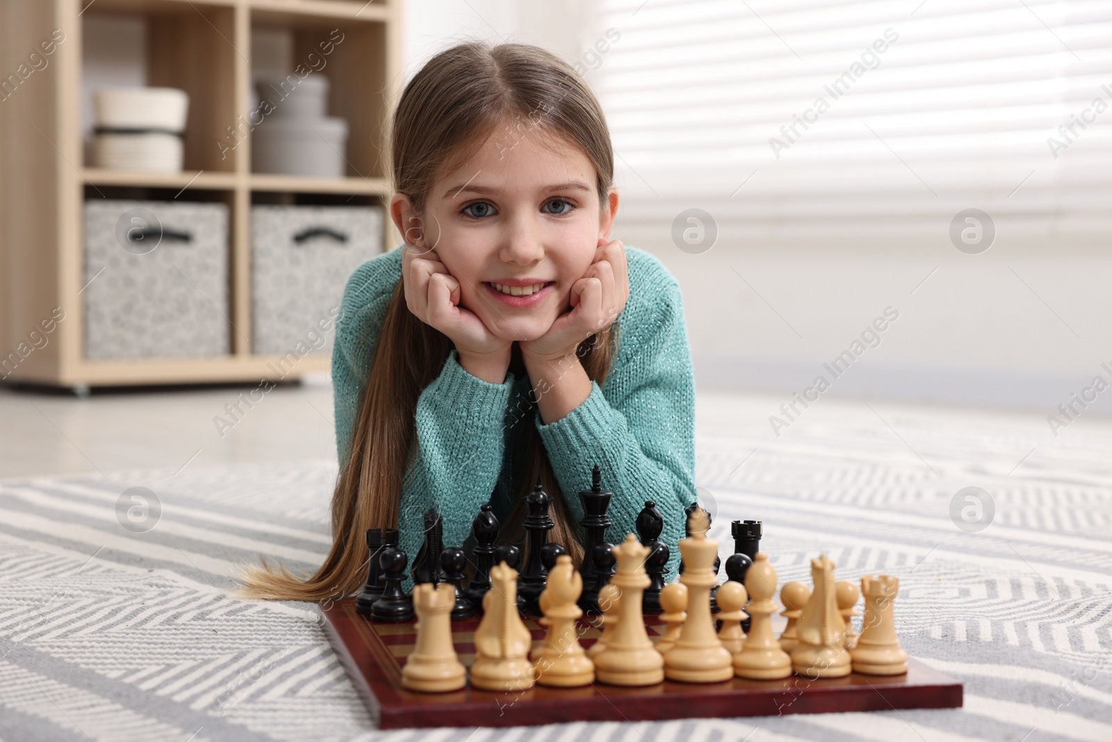 Photo of Cute girl playing chess on floor in room