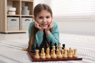 Photo of Cute girl playing chess on floor in room