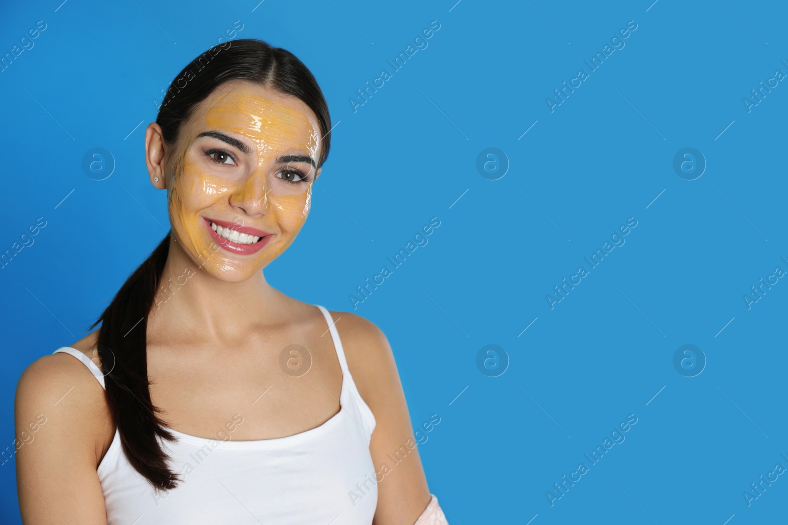 Photo of Young woman with cleansing mask on her face against color background, space for text. Skin care